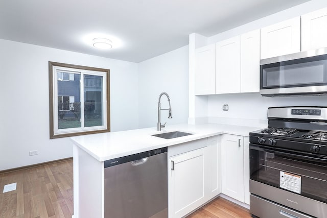 kitchen with sink, light wood-type flooring, appliances with stainless steel finishes, and white cabinetry