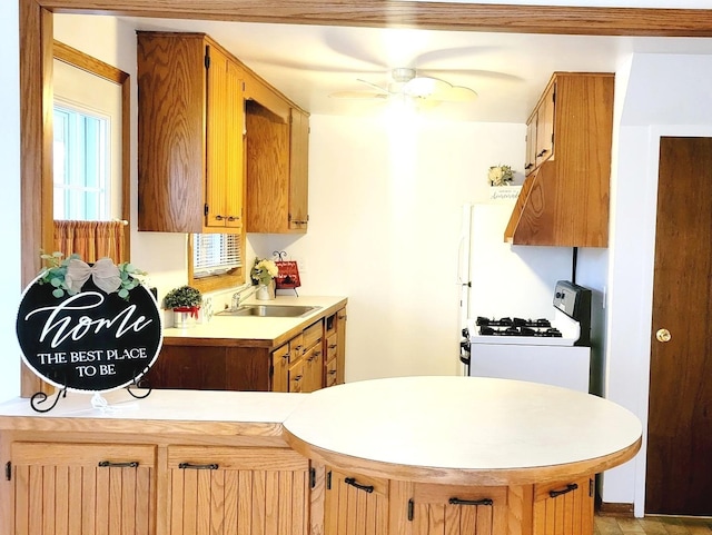 kitchen with white gas stove, ceiling fan, kitchen peninsula, and sink