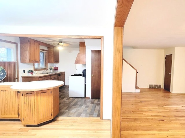 kitchen with premium range hood, sink, white gas range oven, ceiling fan, and light hardwood / wood-style floors