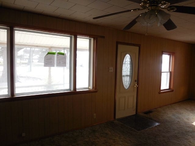 carpeted entrance foyer featuring ceiling fan and wood walls