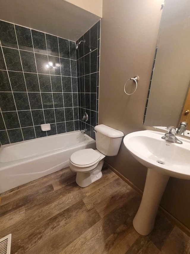 full bathroom with sink, wood-type flooring, tiled shower / bath combo, and toilet