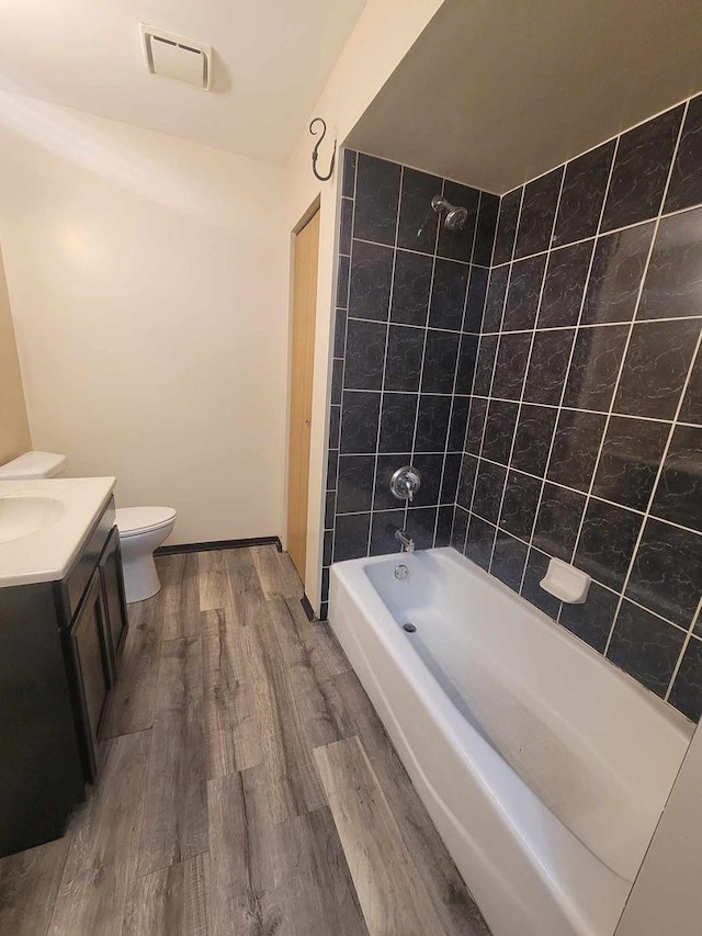 full bathroom featuring vanity, wood-type flooring, tiled shower / bath combo, and toilet