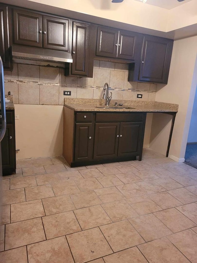 kitchen featuring light stone countertops, dark brown cabinets, light tile patterned flooring, and sink