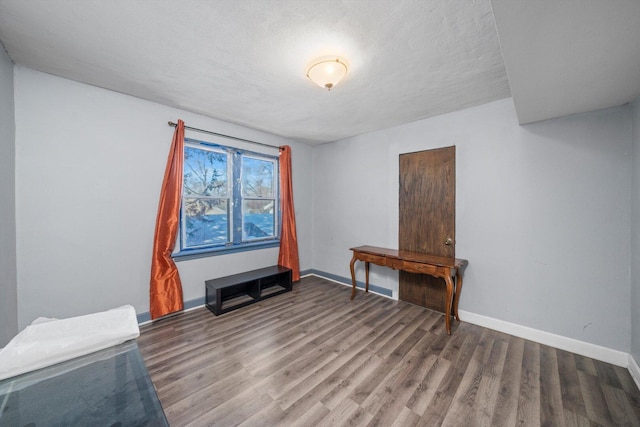 interior space with a textured ceiling, baseboards, and wood finished floors