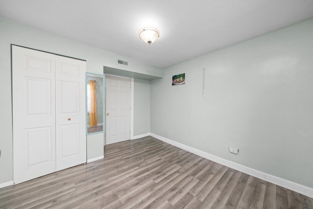 unfurnished bedroom with a closet, visible vents, baseboards, and wood finished floors