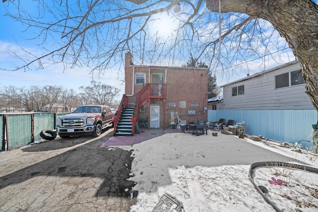 snow covered house featuring a patio, stairway, a chimney, and fence