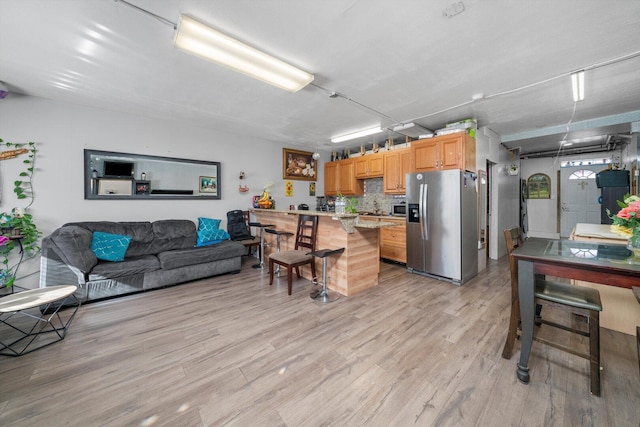 kitchen featuring a breakfast bar area, light wood-style flooring, light countertops, appliances with stainless steel finishes, and tasteful backsplash