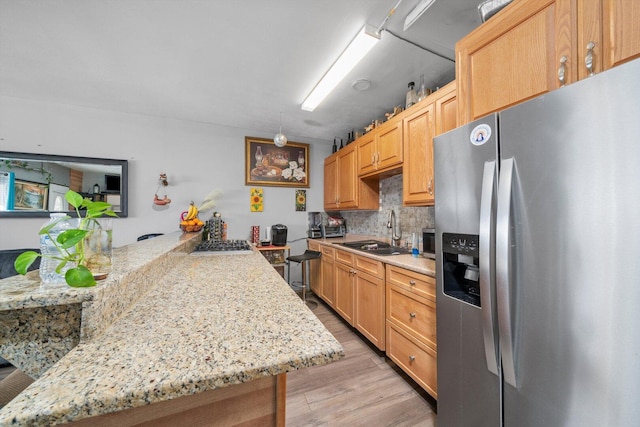 kitchen with decorative backsplash, appliances with stainless steel finishes, light wood-style floors, a sink, and a peninsula