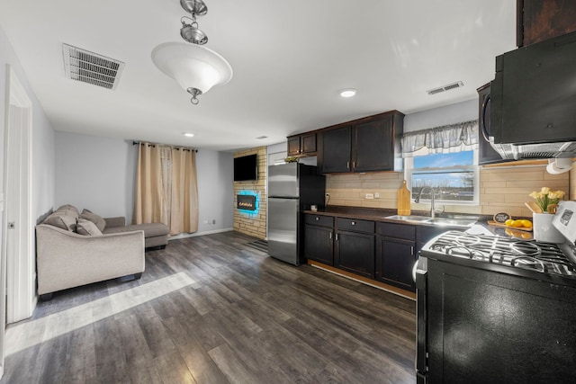 kitchen featuring black / electric stove, sink, dark hardwood / wood-style floors, tasteful backsplash, and stainless steel refrigerator