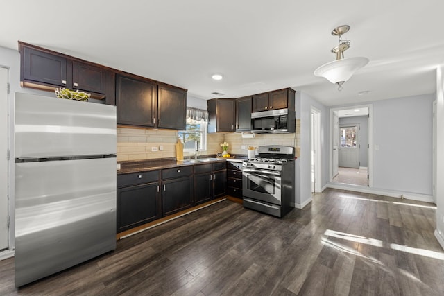 kitchen featuring sink, hanging light fixtures, dark brown cabinets, dark hardwood / wood-style flooring, and stainless steel appliances