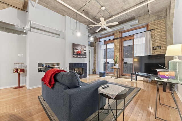 living room with hardwood / wood-style flooring, ceiling fan, and a tiled fireplace