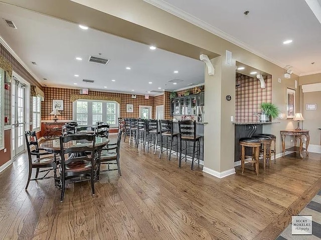 dining room featuring hardwood / wood-style floors, ornamental molding, french doors, and bar area