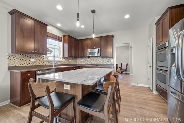 kitchen with a kitchen island, decorative light fixtures, stainless steel appliances, light stone countertops, and light wood-type flooring