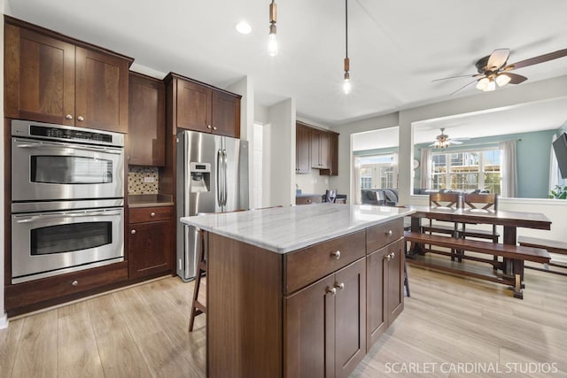 kitchen featuring appliances with stainless steel finishes, hanging light fixtures, light stone counters, dark brown cabinetry, and light hardwood / wood-style floors