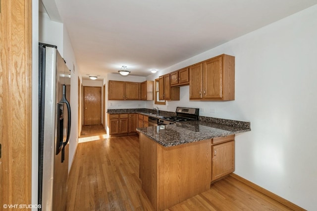 kitchen featuring kitchen peninsula, dark stone countertops, light wood-type flooring, and appliances with stainless steel finishes