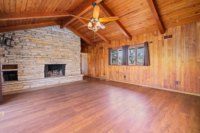 unfurnished living room with vaulted ceiling with beams, wooden walls, ceiling fan, a fireplace, and hardwood / wood-style floors