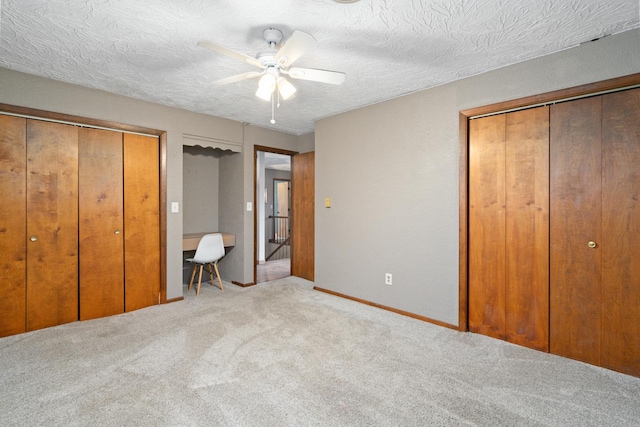 unfurnished bedroom featuring built in desk, carpet floors, a textured ceiling, and two closets