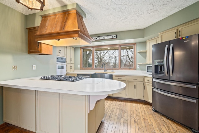 kitchen with sink, a breakfast bar, black appliances, custom exhaust hood, and kitchen peninsula