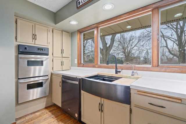 kitchen with sink, light hardwood / wood-style flooring, dishwasher, cream cabinets, and stainless steel double oven