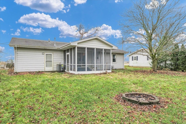 rear view of property featuring a fire pit, a sunroom, central air condition unit, and a lawn