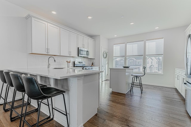 kitchen with appliances with stainless steel finishes, sink, white cabinets, and a kitchen breakfast bar