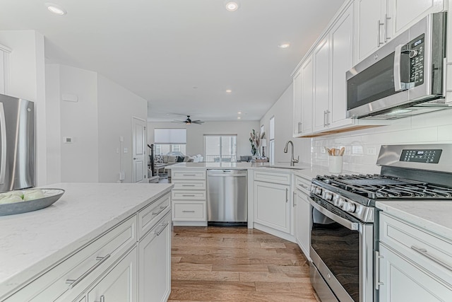 kitchen with sink, stainless steel appliances, light hardwood / wood-style floors, decorative backsplash, and white cabinets