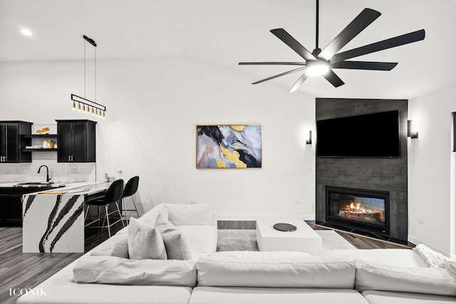 living room with ceiling fan, sink, dark wood-type flooring, vaulted ceiling, and a fireplace