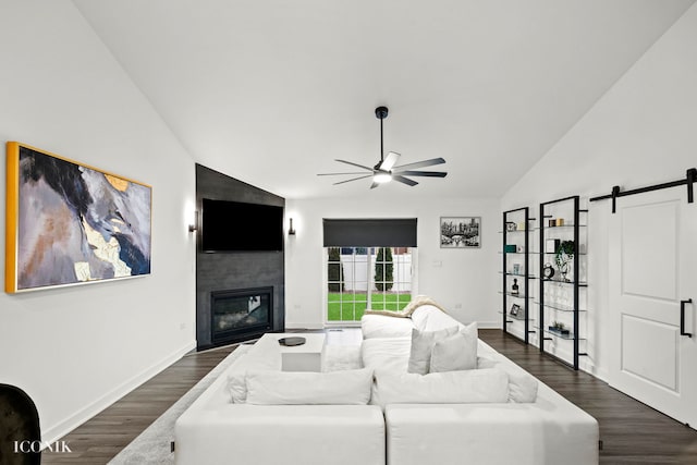 living room featuring ceiling fan, a large fireplace, dark wood-type flooring, a barn door, and lofted ceiling