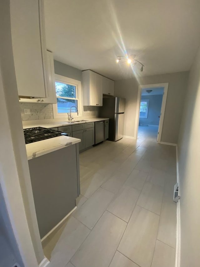 kitchen featuring gray cabinetry, backsplash, rail lighting, sink, and stainless steel appliances