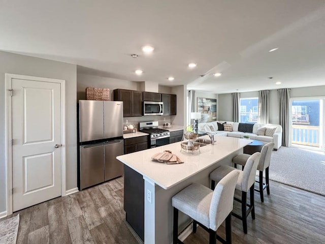 kitchen with a kitchen bar, dark brown cabinets, stainless steel appliances, a kitchen island with sink, and light hardwood / wood-style floors