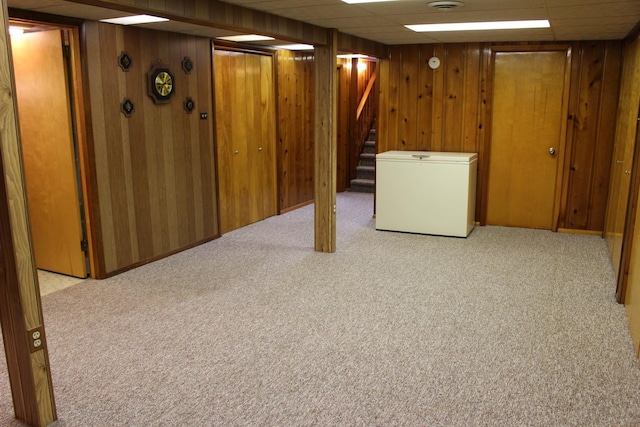 basement featuring wooden walls, refrigerator, light carpet, and a drop ceiling