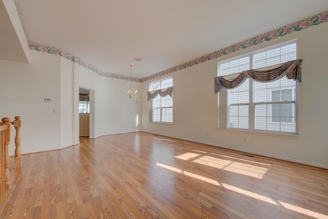 unfurnished room featuring a notable chandelier and light wood-type flooring