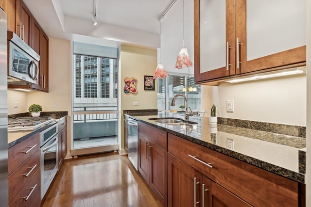 kitchen with rail lighting, stainless steel appliances, sink, pendant lighting, and dark stone countertops