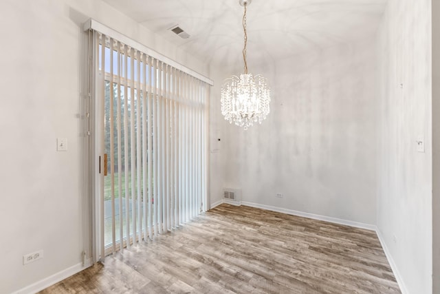 unfurnished dining area with wood-type flooring and an inviting chandelier