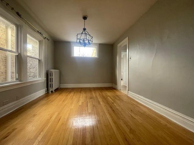 unfurnished dining area with radiator heating unit, a chandelier, and light hardwood / wood-style flooring