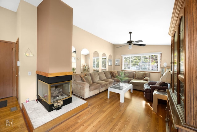 living room featuring ceiling fan, a multi sided fireplace, light wood-type flooring, and vaulted ceiling