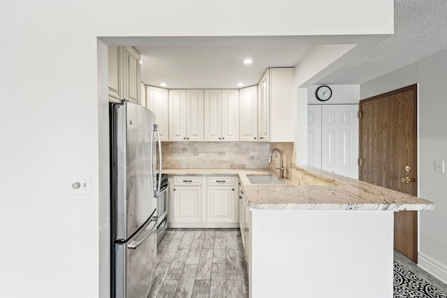 kitchen with backsplash, sink, kitchen peninsula, white cabinetry, and stainless steel appliances