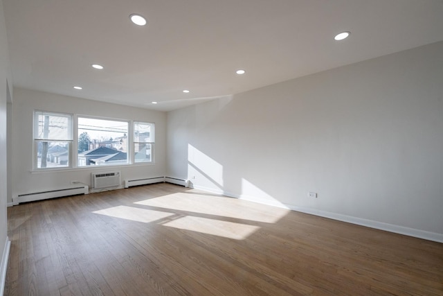 empty room with an AC wall unit, light hardwood / wood-style flooring, and a baseboard heating unit