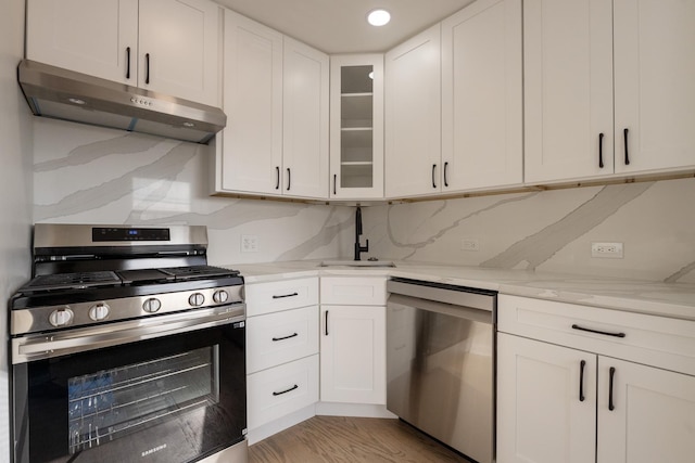 kitchen with light stone countertops, decorative backsplash, stainless steel appliances, light hardwood / wood-style flooring, and white cabinetry