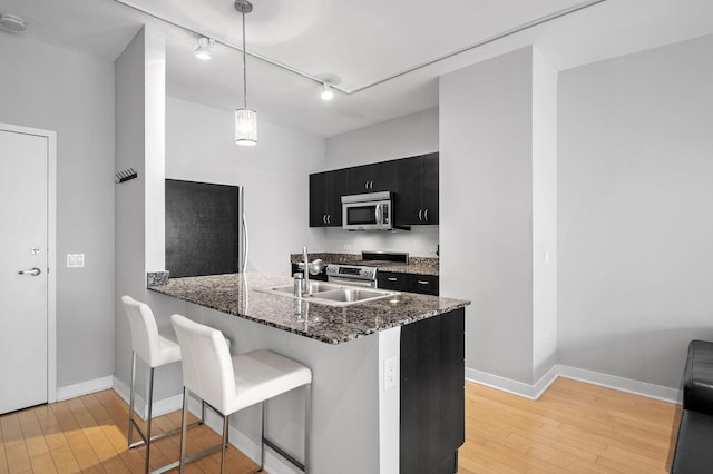 kitchen featuring hanging light fixtures, light wood-type flooring, appliances with stainless steel finishes, a kitchen bar, and kitchen peninsula