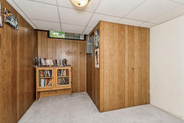 hallway featuring a paneled ceiling, wooden walls, and light colored carpet