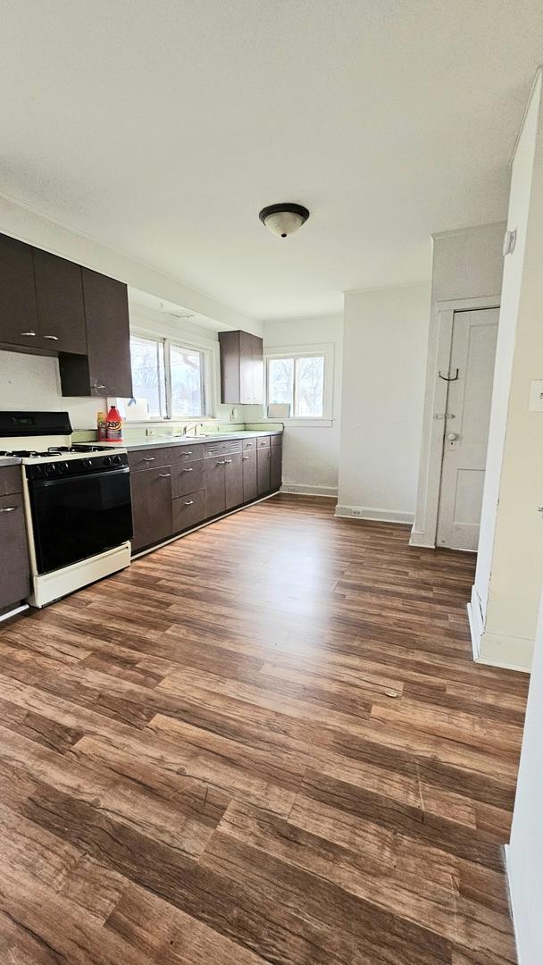 kitchen with baseboards, light countertops, dark wood-style flooring, and gas stove