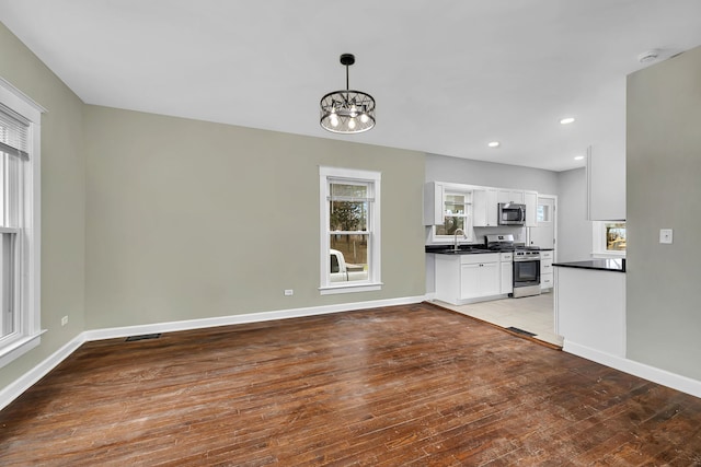 unfurnished living room featuring plenty of natural light, wood-type flooring, sink, and an inviting chandelier