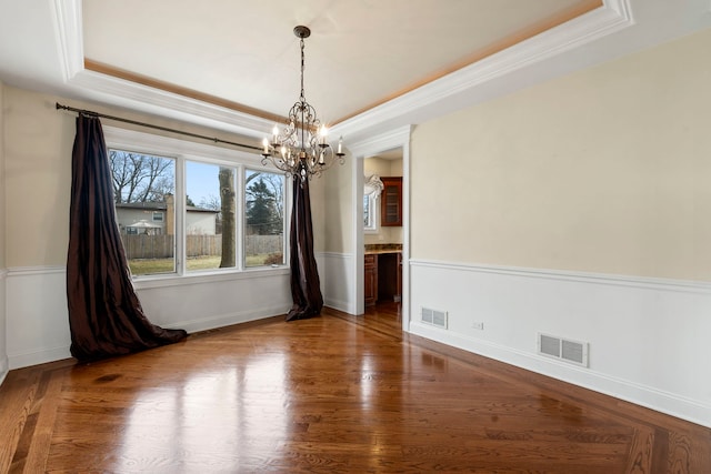 unfurnished dining area featuring a chandelier, dark hardwood / wood-style floors, crown molding, and a tray ceiling