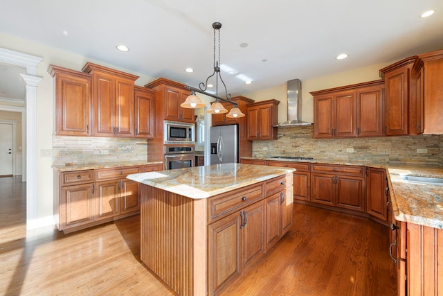 kitchen with backsplash, wall chimney exhaust hood, stainless steel appliances, a kitchen island, and hanging light fixtures