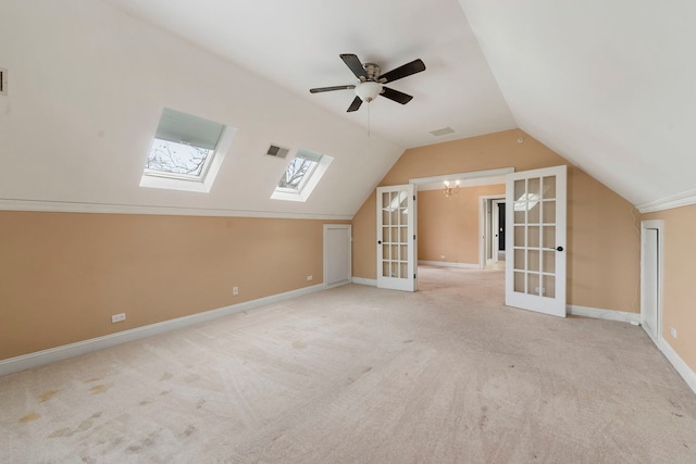 additional living space with vaulted ceiling with skylight, ceiling fan with notable chandelier, light colored carpet, and french doors