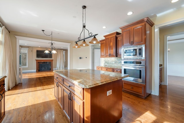 kitchen with decorative backsplash, stainless steel appliances, pendant lighting, wood-type flooring, and a kitchen island