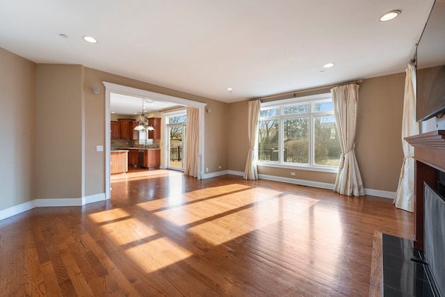 unfurnished living room featuring a notable chandelier, light wood-type flooring, and a wealth of natural light