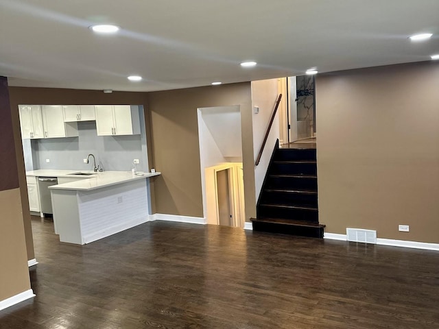 kitchen with white cabinetry, kitchen peninsula, dark wood-type flooring, stainless steel dishwasher, and sink