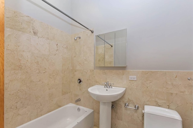 bathroom featuring tiled shower / bath combo, toilet, and tile walls